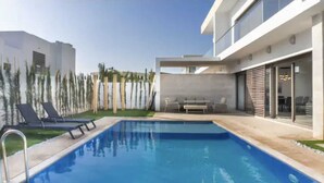 Un área de piscina moderna con una piscina azul cristalina, sillas de descanso y una mesa de patio.