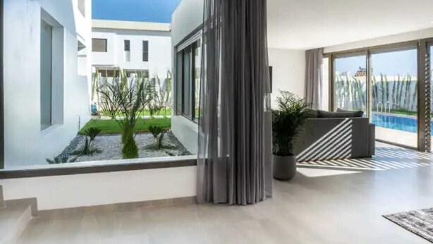 Una sala de estar moderna con un amplio ventanal, vista a una piscina y un balcón.