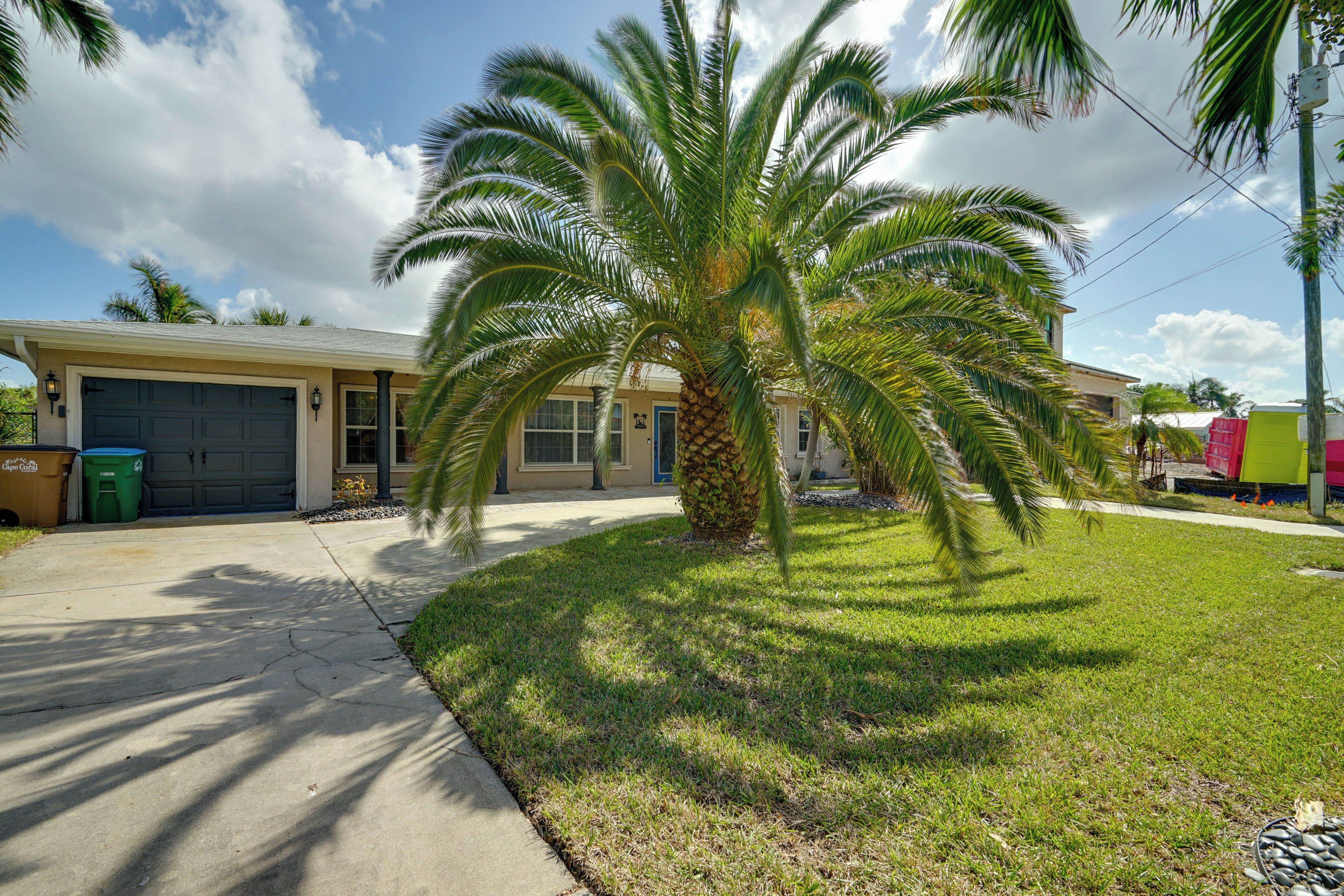 A residential house with a garage, a lawn, and a palm tree.