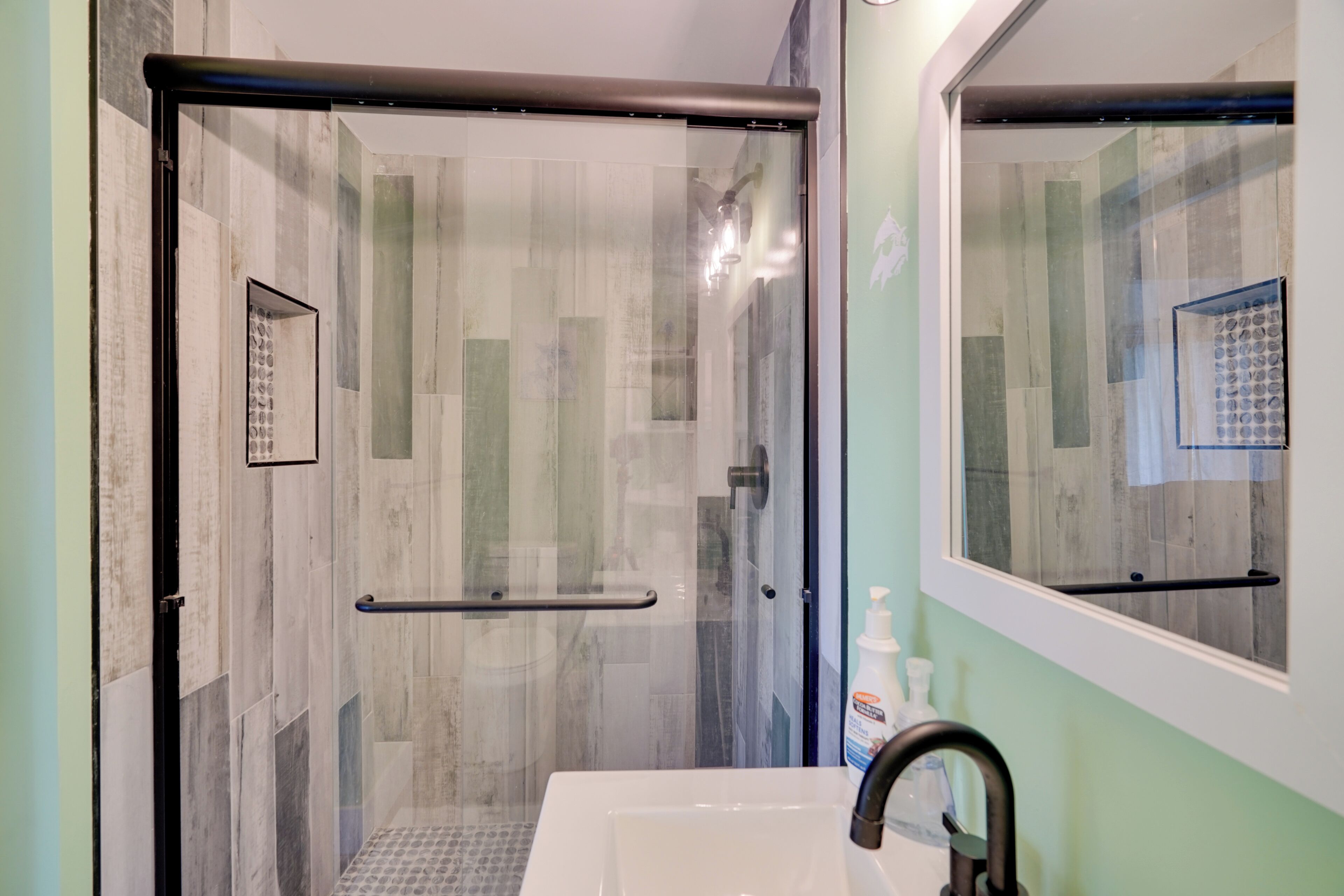 A bathroom with a glass-enclosed shower, a white sink, and a mirror.