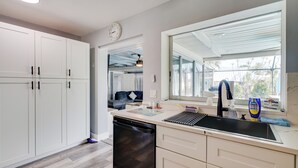 A modern kitchen with white cabinets, a black dishwasher, and a large window providing natural light. - < 1 Mi to Four Freedoms Beach: Canal-front Getaway (Cape Coral)