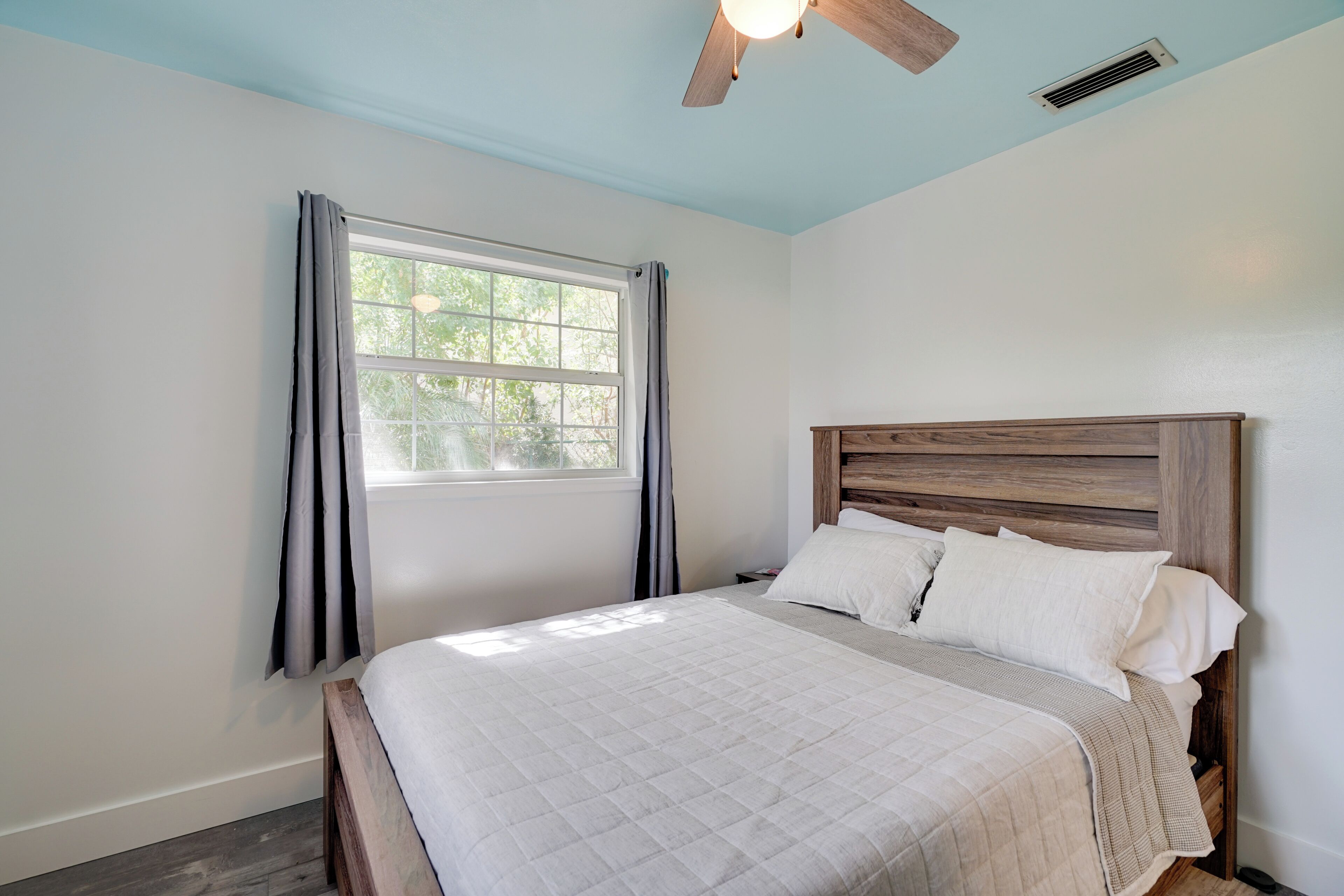 A bedroom with a bed, a window with curtains, a ceiling fan, and a wooden headboard.