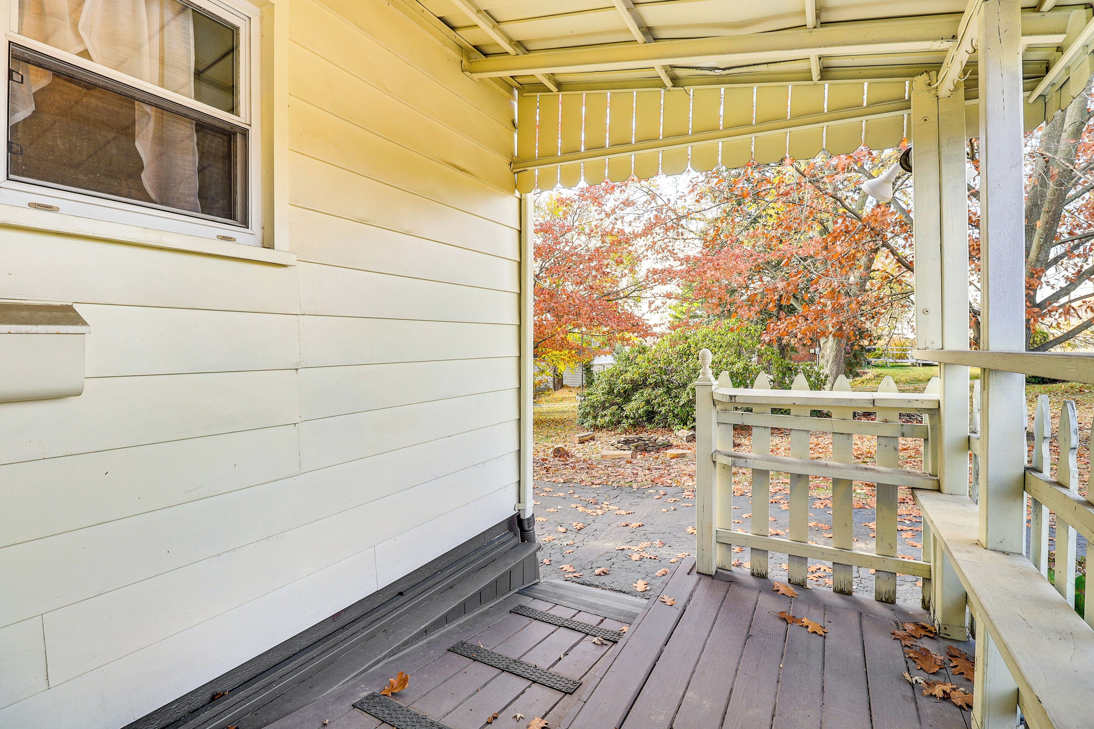 A porch with a wooden railing and a view of trees with autumn leaves.