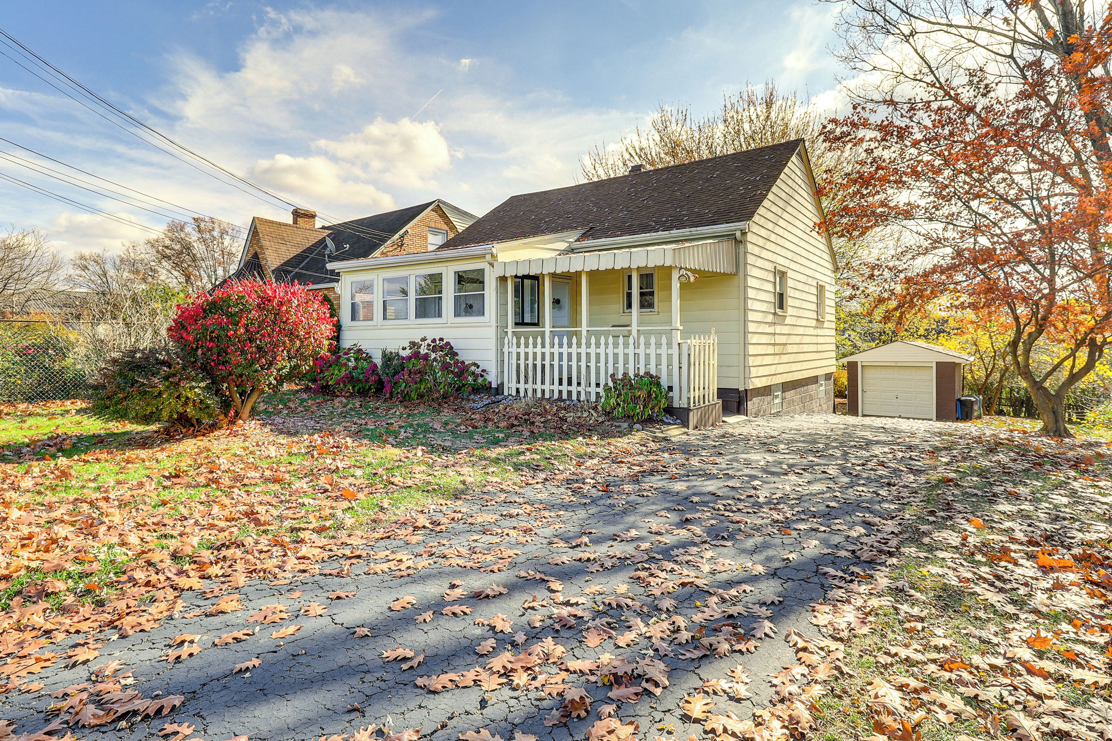 A two-story house with a front porch, a garage, and a yard with fallen leaves.