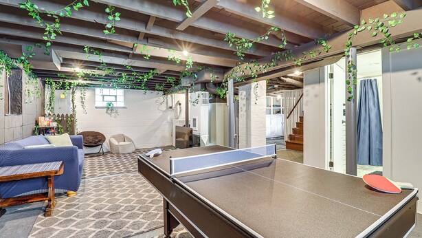 A ping pong table in a room with a patterned rug, a sofa, and hanging plants. - Game Room & Fire Pit: West Mifflin Home! (West Mifflin)
