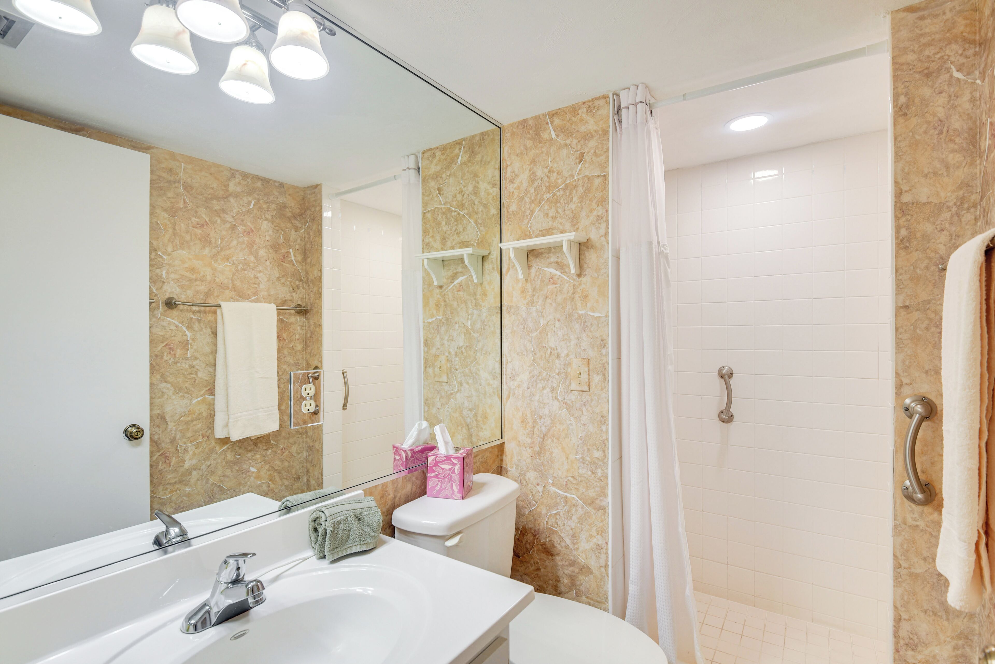 A bathroom with a sink, mirror, toilet, and shower.