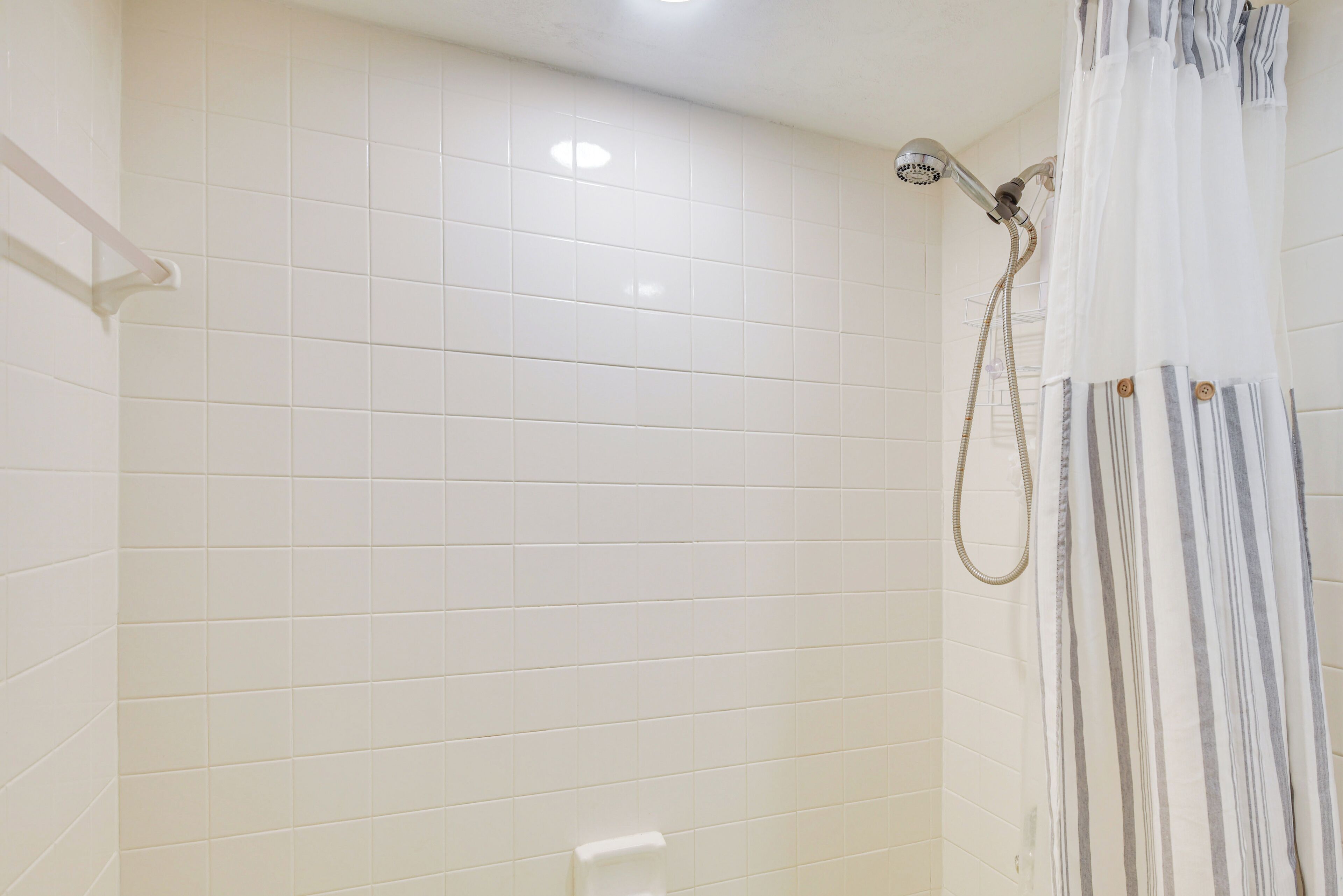 A bathroom with white tiled walls, a shower with a curtain, and a towel rack.