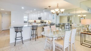 A modern kitchen with white cabinets, a central island with bar stools, and a dining area with a glass table and white chairs.