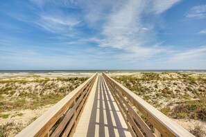 Une promenade en bois menant à une plage bordée de dunes, sous un ciel dégagé.