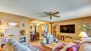 A spacious living room with a ceiling fan, a television, and a dining area with a chandelier. - Cyclists' Haven: Southwestern-style Home in Tucson (Tucson)