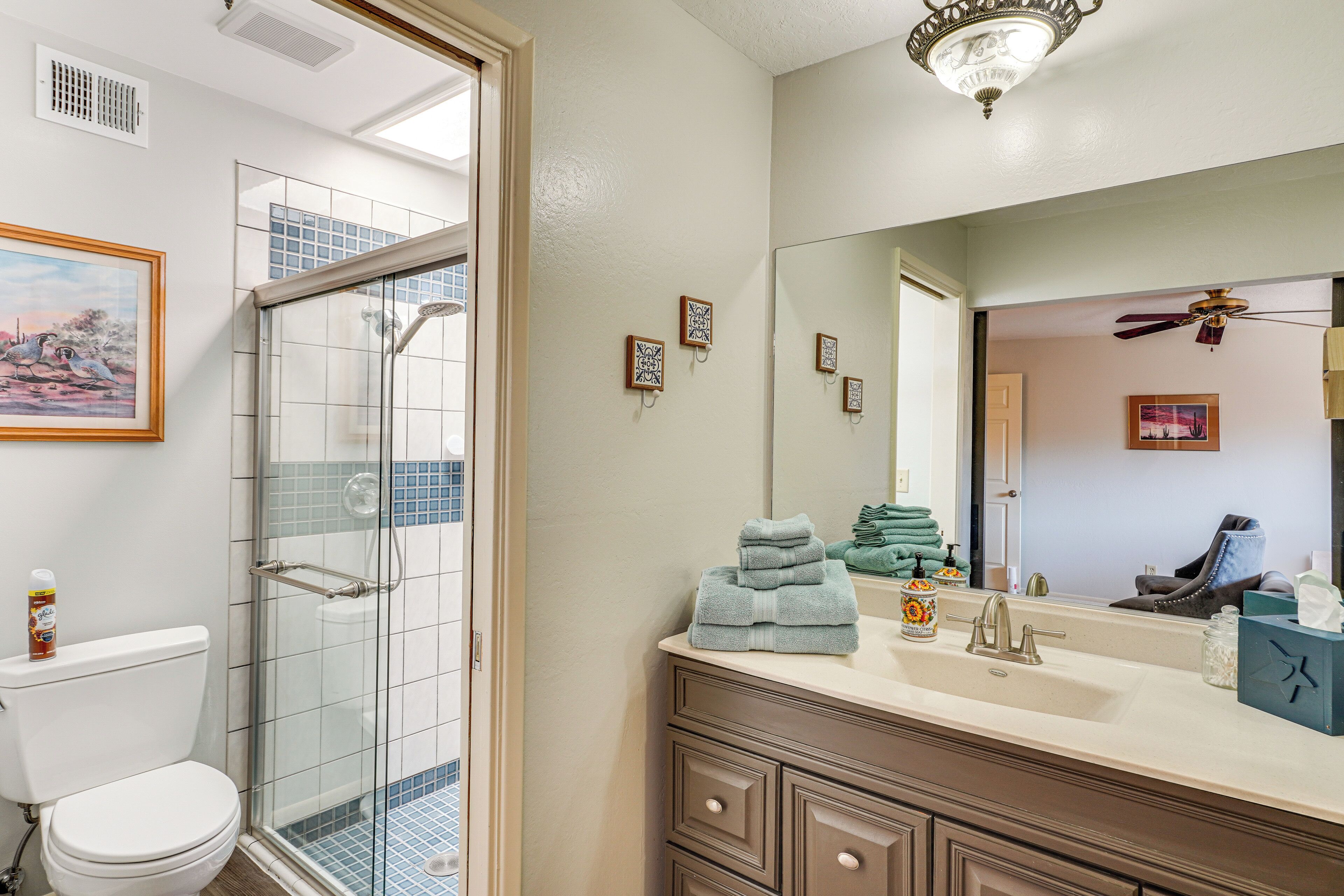 Une salle de bain avec une douche à parois de verre, des toilettes, un lavabo avec un miroir et un ventilateur de plafond.