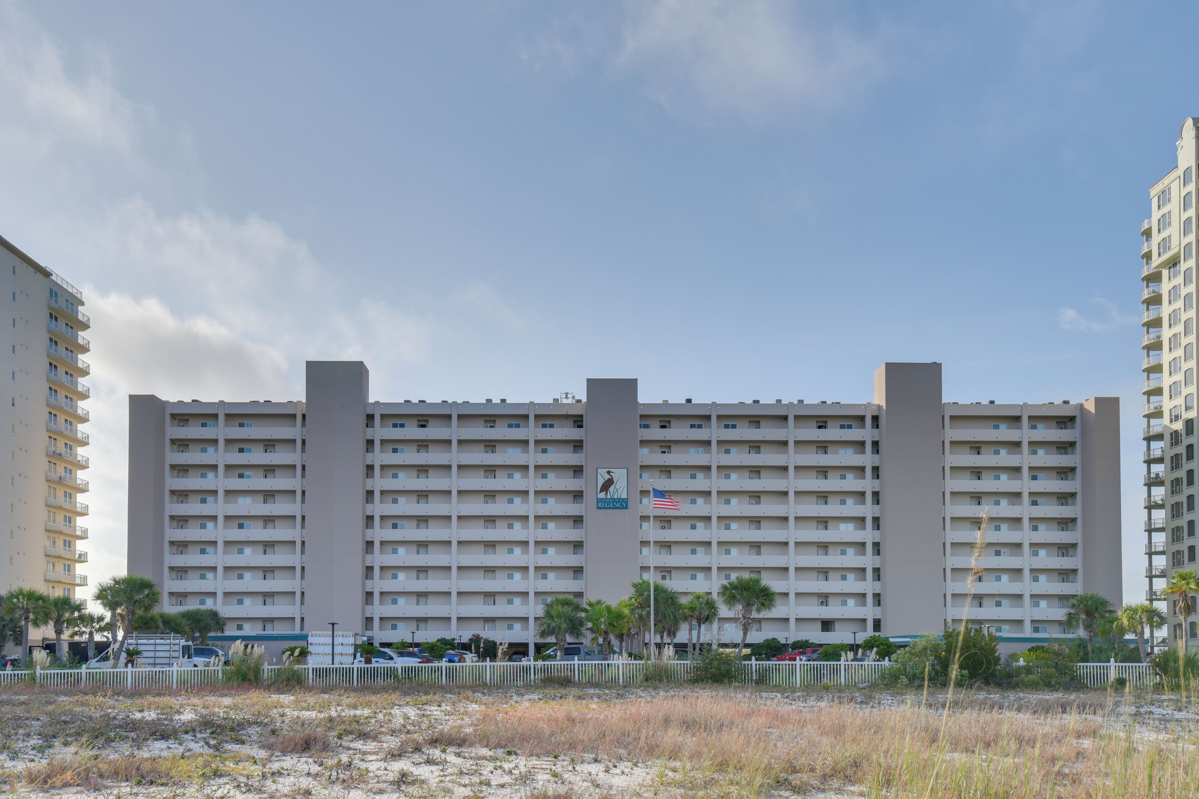 Un grand hôtel à plusieurs étages, avec un drapeau, et une plage au premier plan.