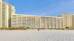 Hotel sulla spiaggia con numerosi balconi, una spiaggia sabbiosa di fronte e un cielo azzurro limpido.