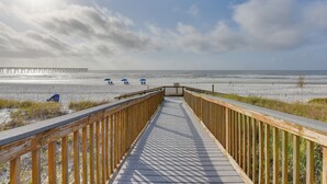 Una passerella di legno che conduce a una spiaggia, con ombrelloni e un molo all'orizzonte.