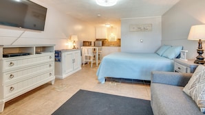 Ein Schlafzimmer mit Bett, Schreibtisch, Stuhl, Fernseher und einer Küchenzeile.