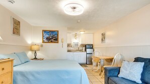 A bedroom with a bed, a dresser, a nightstand, a lamp, a blue sofa, and a dining area with a table and chairs. - 'beachfront 15' Condo on Old Orchard Beach (Old Orchard Beach)