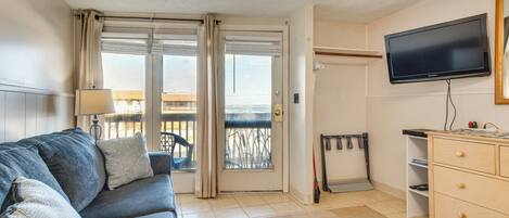 Ein Wohnzimmer mit einer Couch, einem Fernseher, einer Schiebetür zu einem Balkon und einer kleinen Holzeinrichtung.