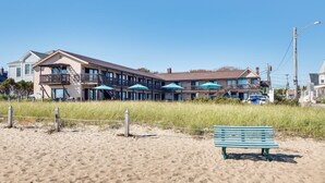 A beachfront hotel with multiple balconies, outdoor umbrellas, and a sandy beach area with a bench. - 'beachfront 16' Condo on Old Orchard Beach (Old Orchard Beach)