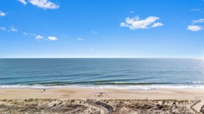 Une plage avec un ciel dégagé, un rivage sablonneux et quelques personnes qui se promènent.