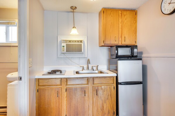 A compact kitchen with wooden cabinets, a built-in microwave, a refrigerator, and a window with blinds. - 'beachfront 13' Condo on Old Orchard Beach (Old Orchard Beach)
