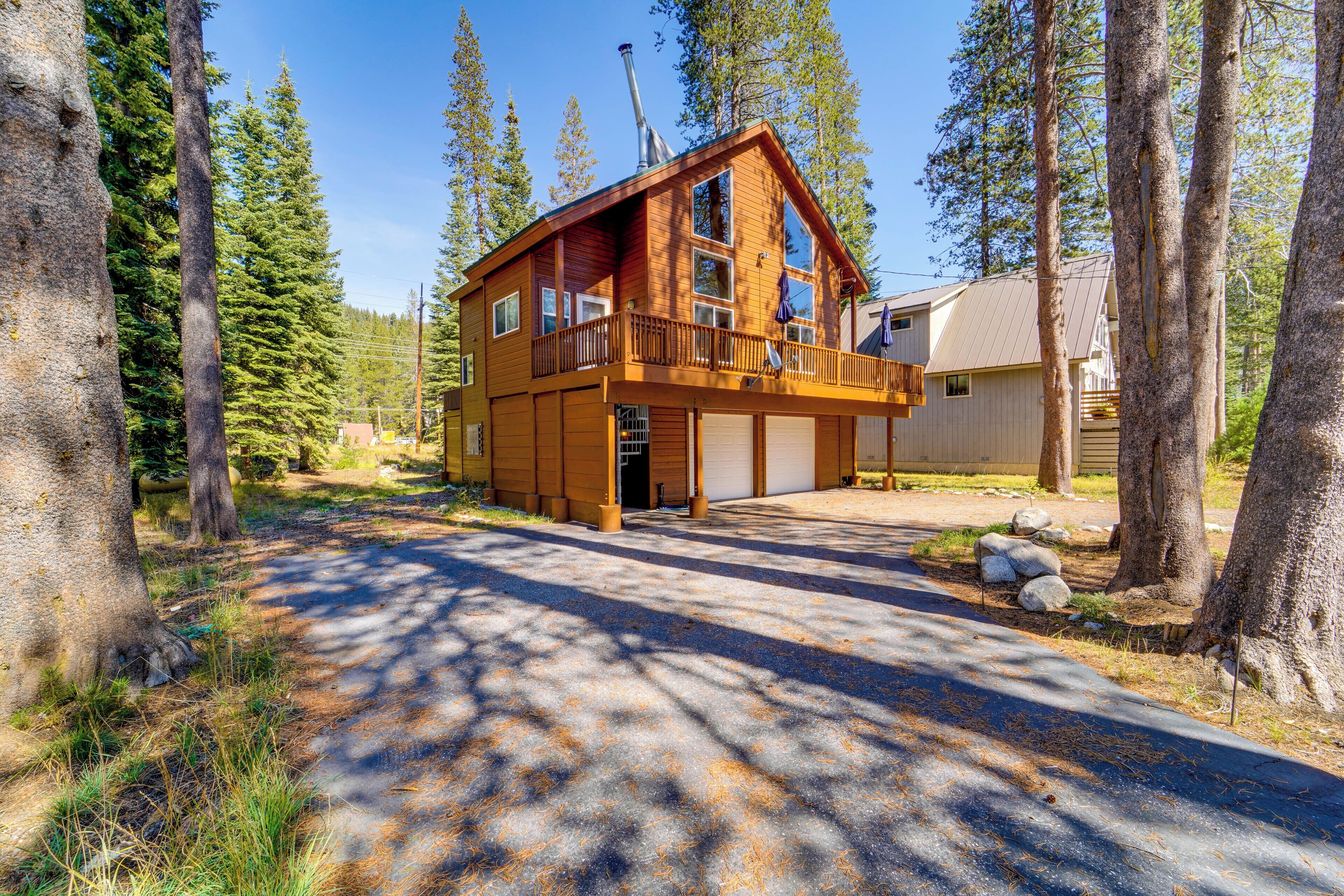 A two-story log cabin with a balcony, surrounded by tall pine trees.