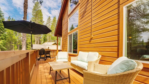 A wooden deck with outdoor furniture, including a table and chairs, and a wicker chair with cushions. - Neighborhood Beach Access! Soda Springs Getaway (Truckee)