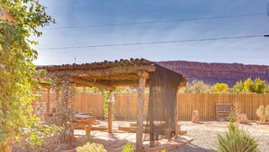 A wooden pergola with a mesh cover, surrounded by a gravel patio, wooden fence, and various plants. - Stunning Views: Quiet Bluff Home Near Hiking! (Bluff)