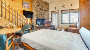 A cozy room with a large bed, wooden staircase, stone wall, fireplace, and a dining area with chairs and a table. - 2 Mi to Granby Ranch: Studio w/ Resort Amenities! (Granby)