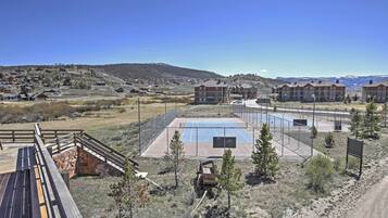 A residential area with a large building complex, a fenced tennis court, and a wooden deck.
