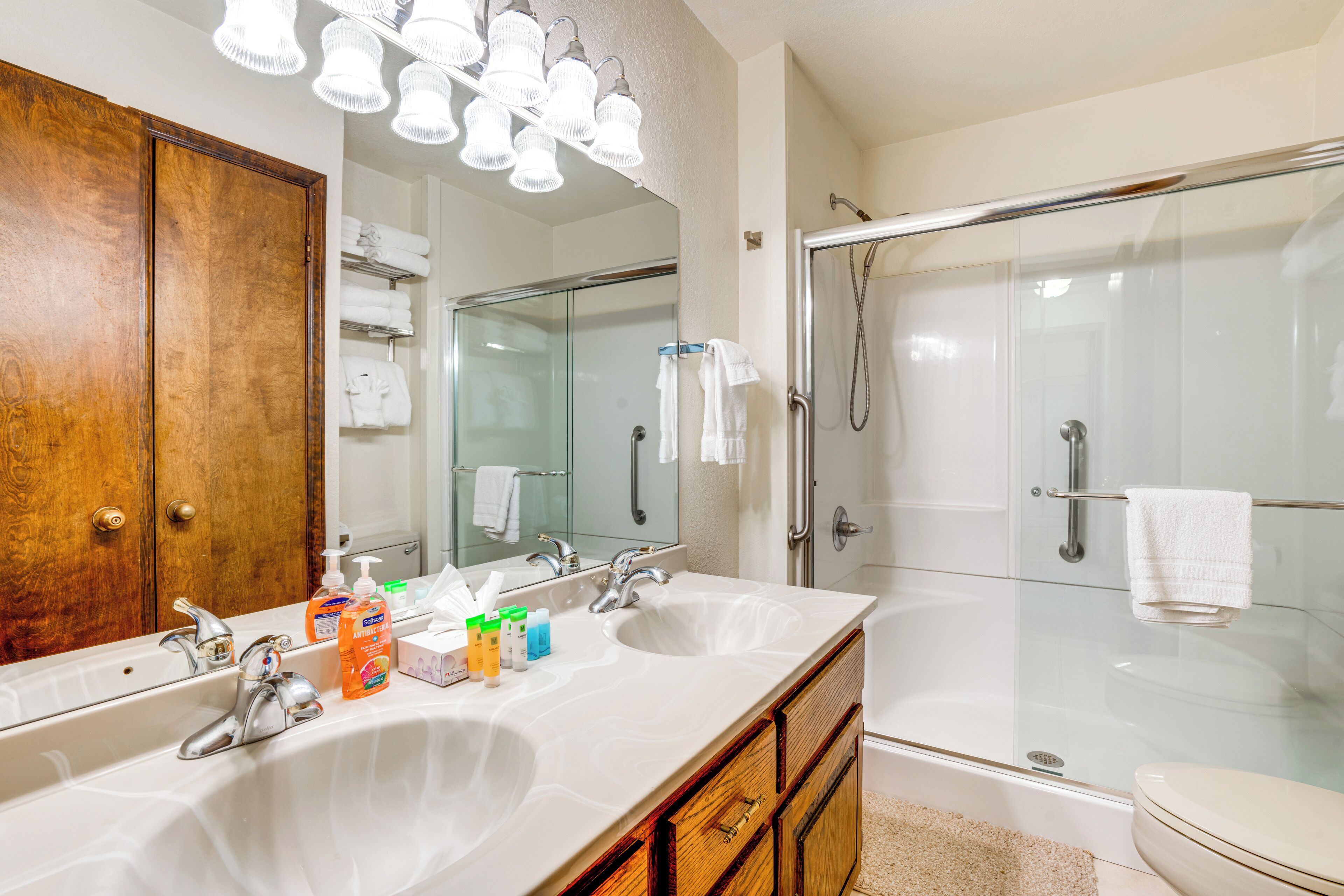 Une salle de bain avec un double vasque, un meuble-lavabo en bois, une cabine de douche en verre et un grand miroir.