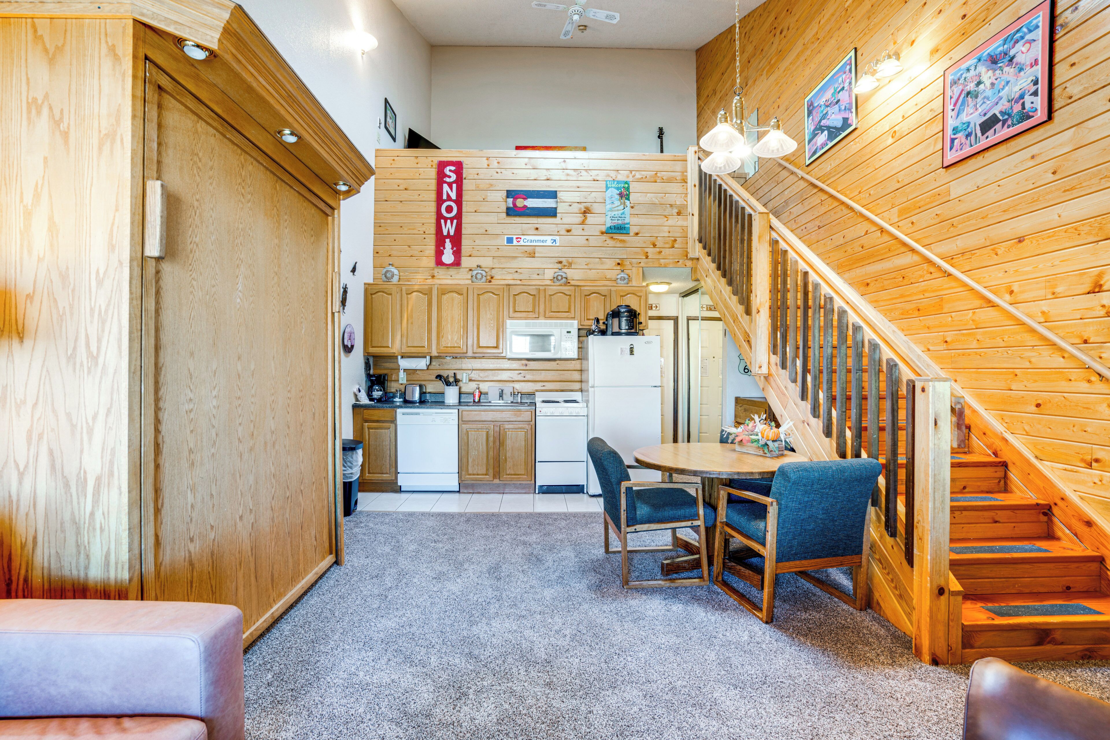 A cozy interior with a wooden staircase, a dining area with chairs, and a kitchen with wooden cabinets and appliances.