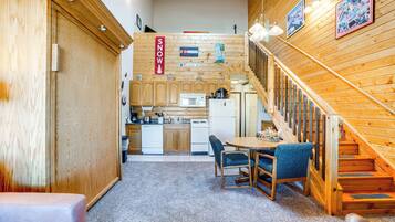 A cozy interior with a wooden staircase, a dining area with chairs, and a kitchen with wooden cabinets and appliances.