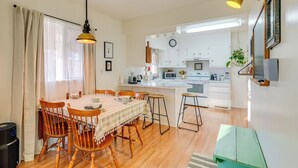 A compact kitchen with white cabinets, a microwave, and a sink. There is a dining area with a table and chairs, and a green bench. - Patio, Grill & Outdoor Dining: Conrad Home! (Conrad)