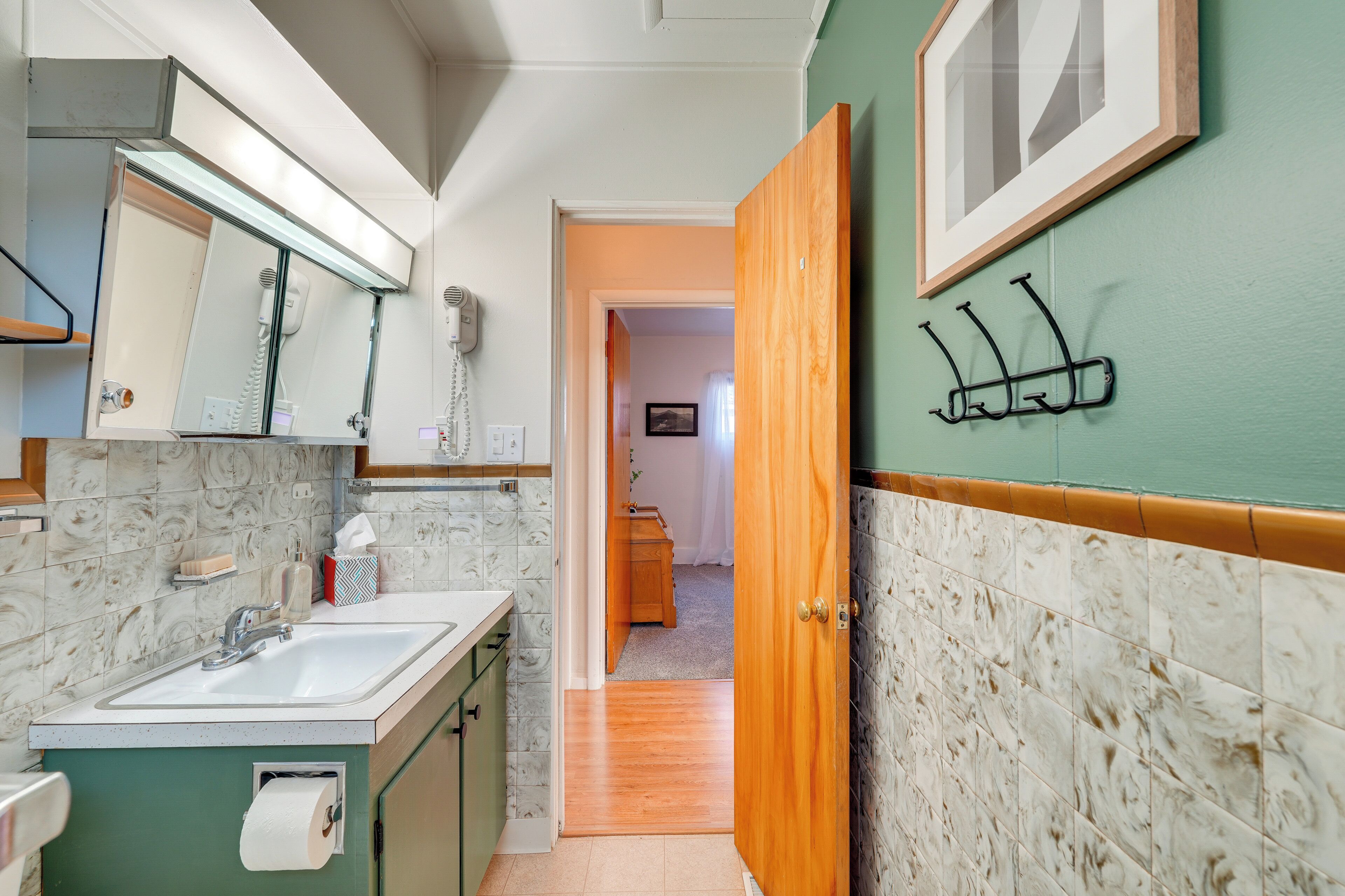 Baño con lavamanos, espejo y dispensador de toallas.