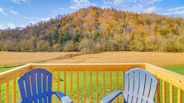 Un pontile di legno con due poltrone Adirondack blu rivolte verso una collina ricoperta da bosco e foglie autunnali.