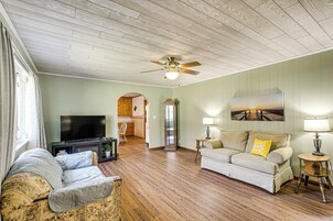 A living room with a sofa, a television, a ceiling fan, and a painting on the wall.