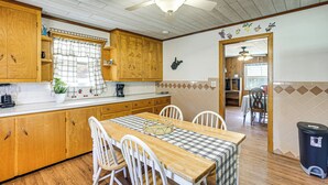 Ett kök med träskåp, ett matbord med stolar, en takfläkt och en papperskorg.