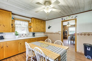 A kitchen with wooden cabinets, a dining table with chairs, a ceiling fan, and a trash can.