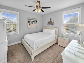 A bedroom with a bed, a ceiling fan, a nightstand, a dresser, and a window with blinds.