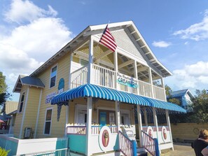 A two-story building with a blue and white striped awning, an American flag, and a sign that reads "Blue Mountain Beach Creamery."