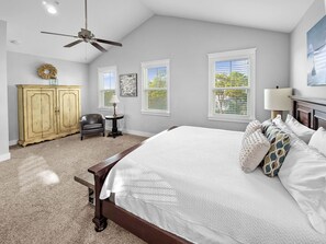 A bedroom with a large bed, a ceiling fan, a wooden cabinet, a chair, and a small table.