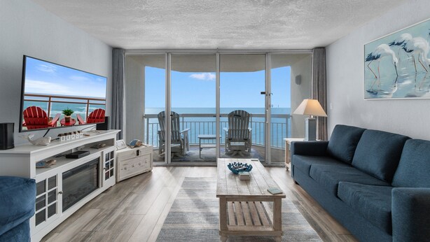 A balcony with a view of the ocean, a television, and seating arrangements.