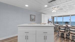 A kitchen with white cabinets, a ceiling fan, and a view of the ocean.
