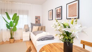 Een slaapkamer met een bed, nachtkastje, lamp en een potplant.