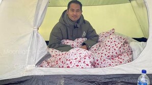 A person sitting inside a tent with a floral-patterned blanket.