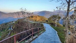 A paved pathway with a metal railing, surrounded by natural vegetation and mountains in the background.