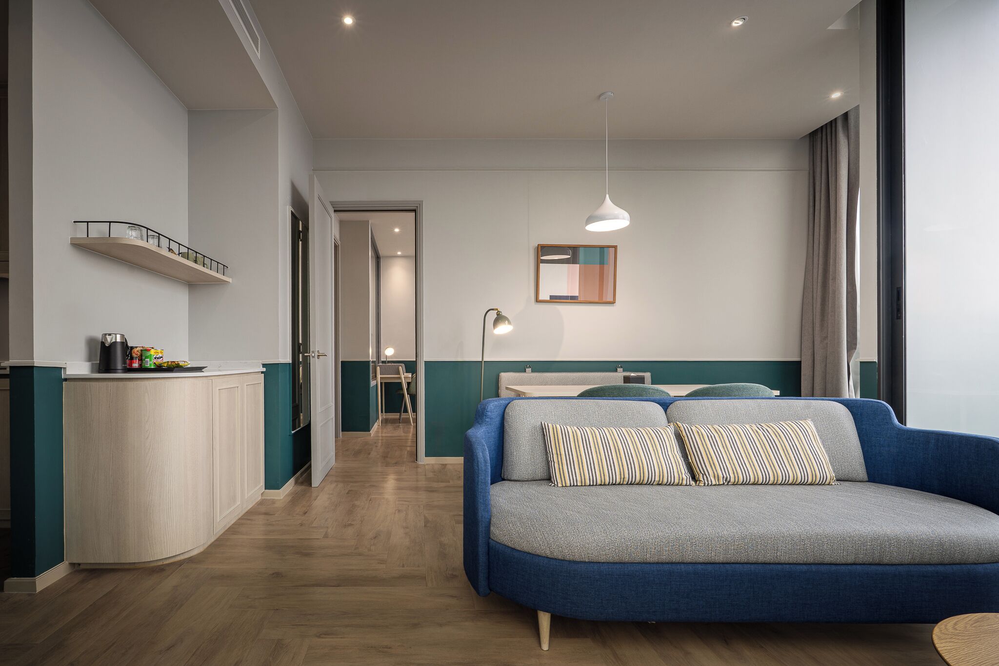 Ein modernes Wohnzimmer mit einem blauen Sofa, einem kleinen Tisch und einer Küchenzeile mit Arbeitsplatte und Schränken.
