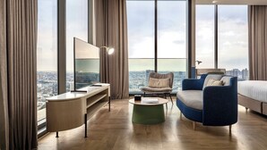 Ein modernes Hotelzimmer mit weitreichendem Stadtblick, einem Schreibtisch mit Flachbildfernseher, einer gemütlichen Couch und einem Bett.