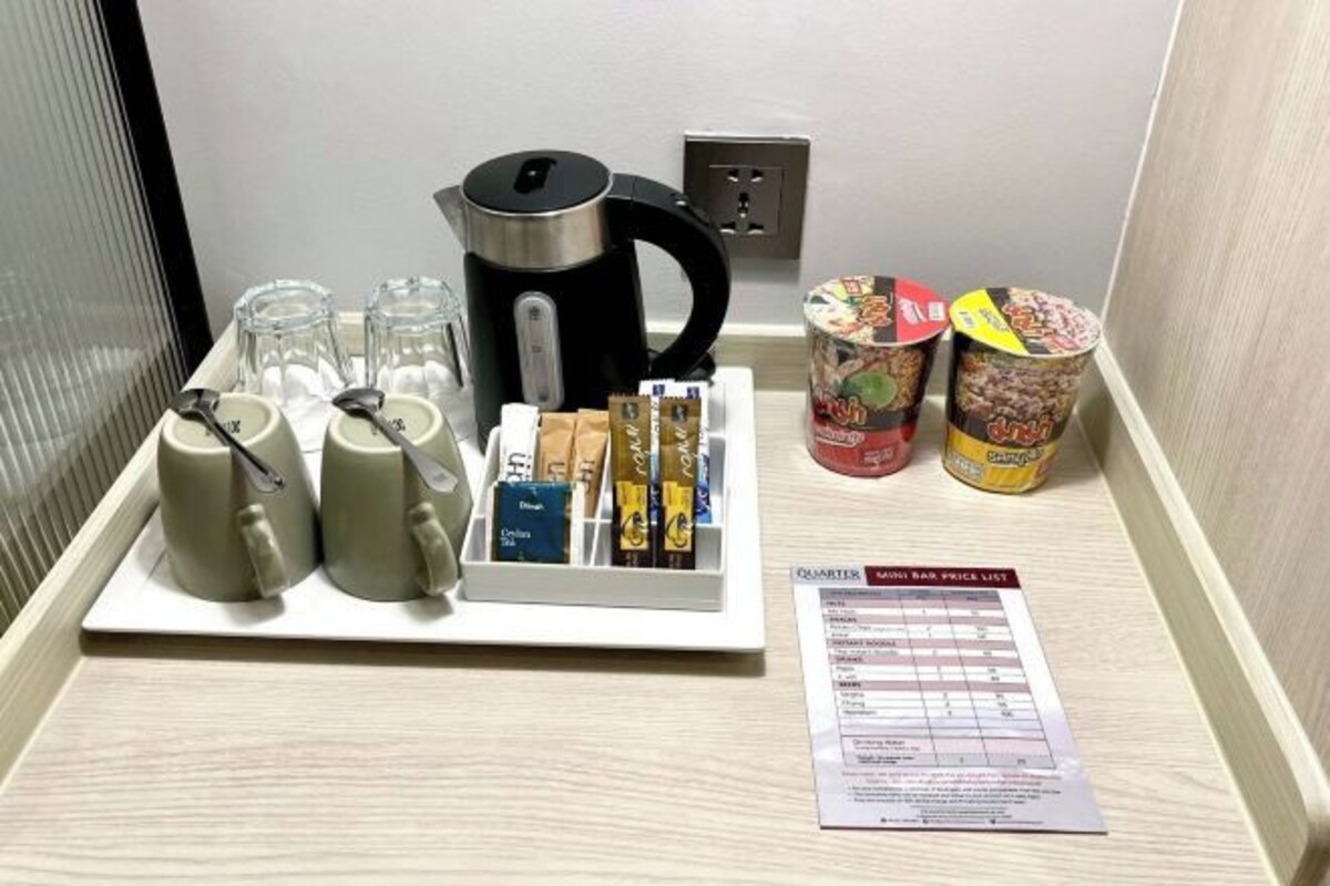 A mini bar setup with a kettle, cups, snacks, and a price list.