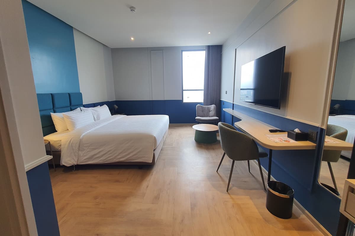 Une chambre d’hôtel moderne équipée d’un grand lit, d’un bureau, d’une chaise, d’une télévision et d’une fenêtre.